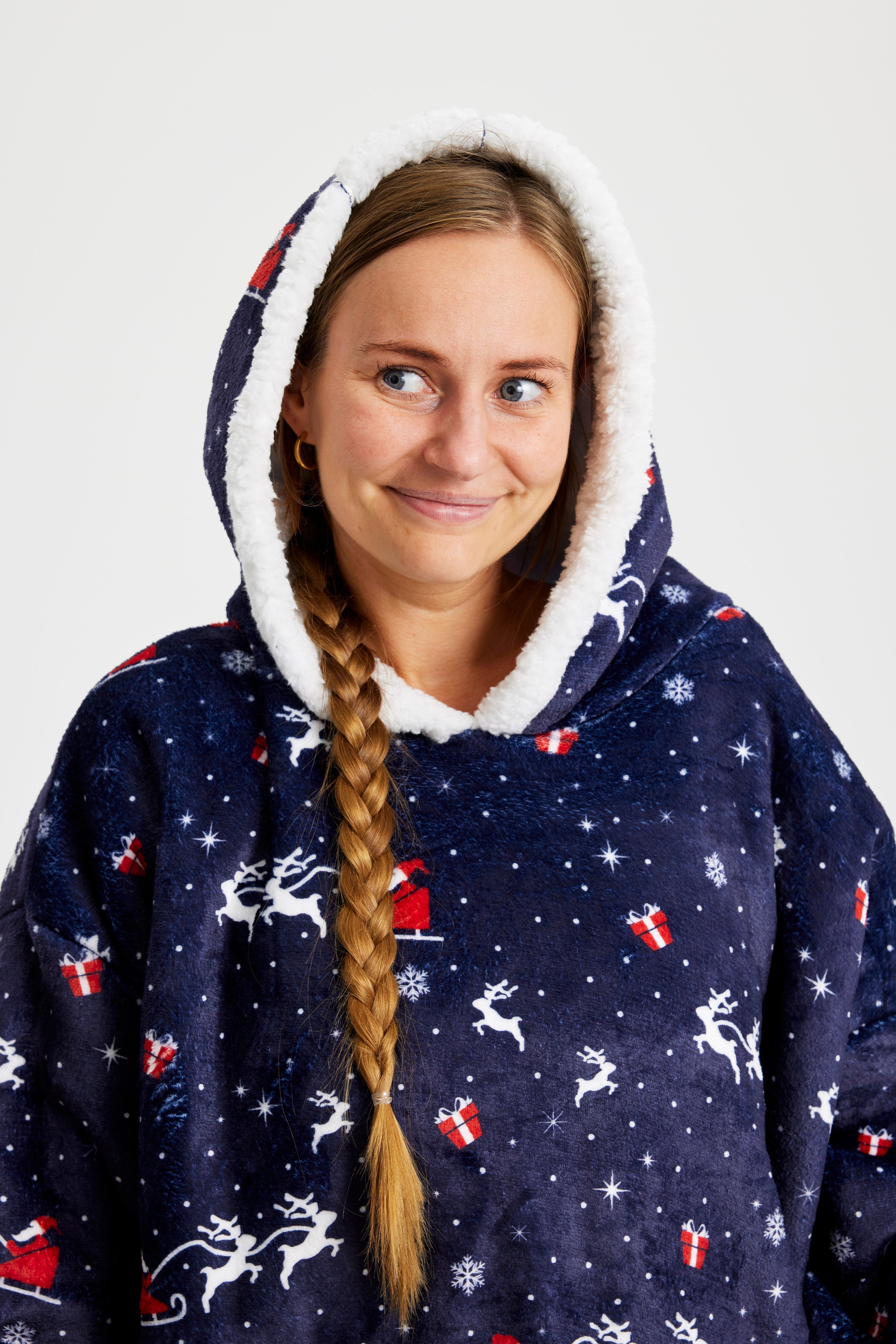 Une femme souriante avec une longue tresse portant un sweat à capuche de Noël bleu foncé.